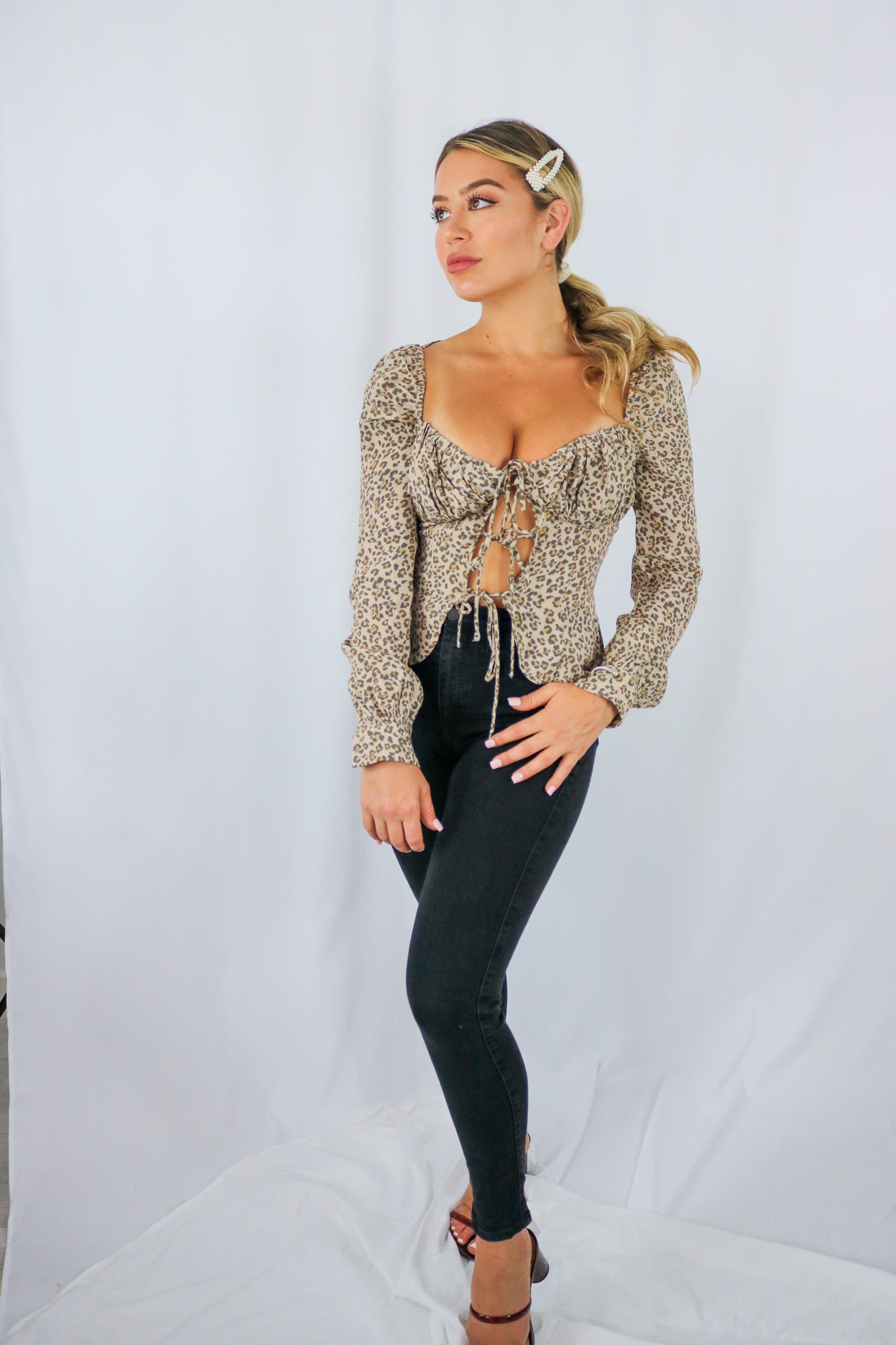 Blonde girl models a leopard print tie blouse for Scarlette The Label, an online fashion boutique for women. The long sleeve leopard blouse is paired with dark denim jeans.