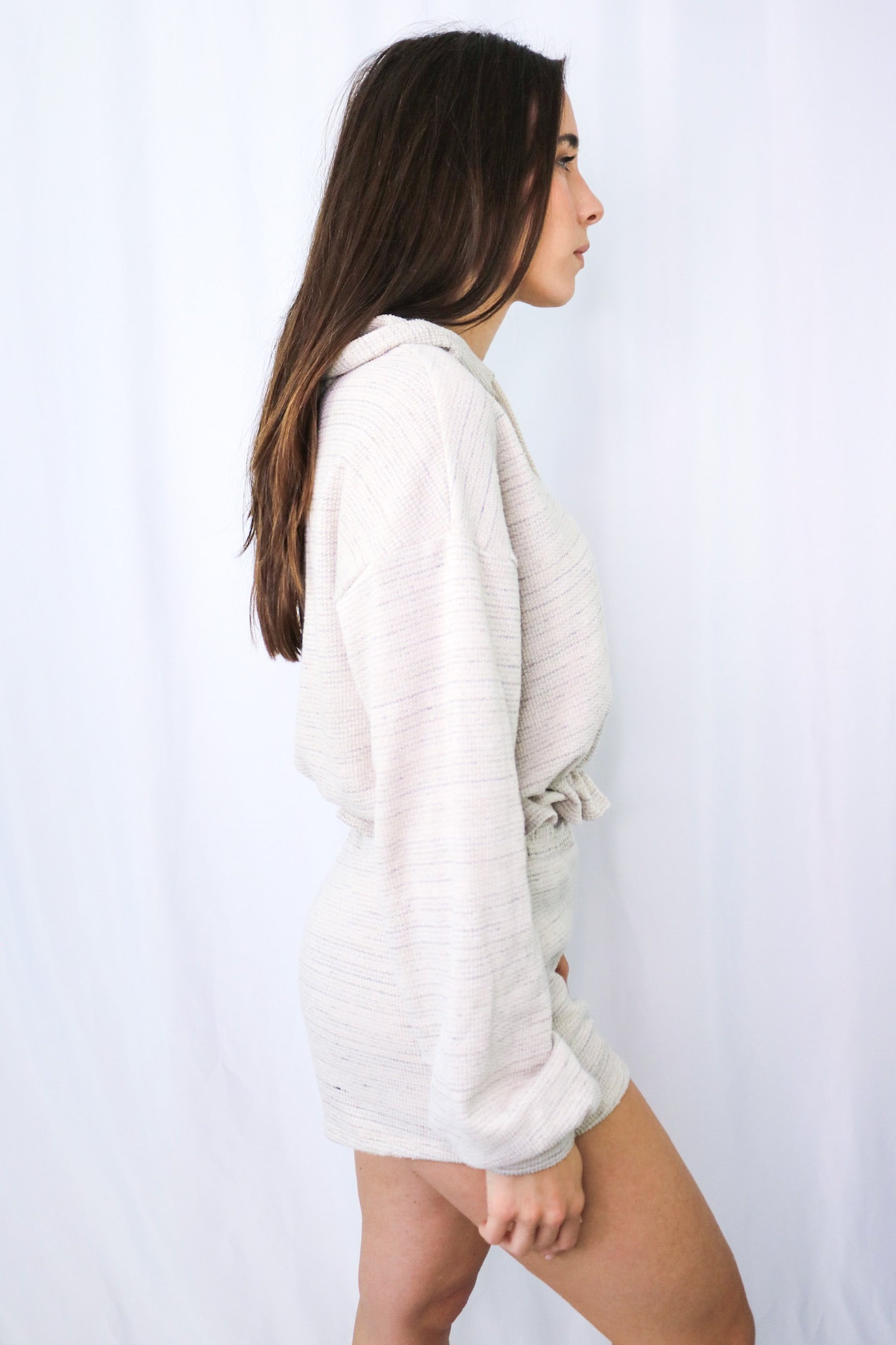 Brunette girl models a long sleeve hooded loungewear short set in color: natural for Scarlette The Label, an online fashion boutique for women.