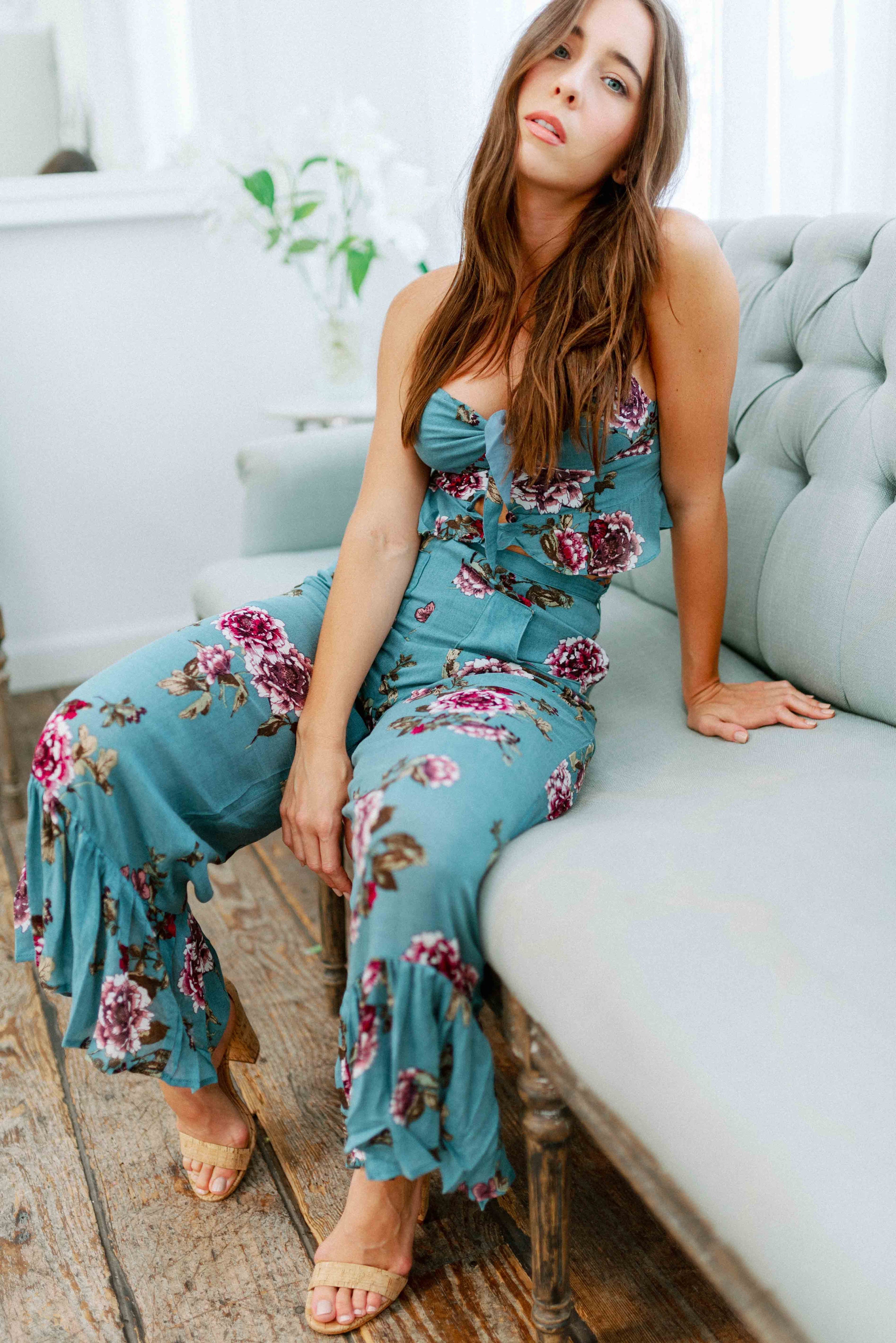Brunette girl models a matching floral pant set (co-ord) for Scarlette The Label, an online boutique for women. The pant set is blue and has floral details. The crop top is a blue spaghetti strap tank top and the pants are blue flare pants. Paired with nude heels.