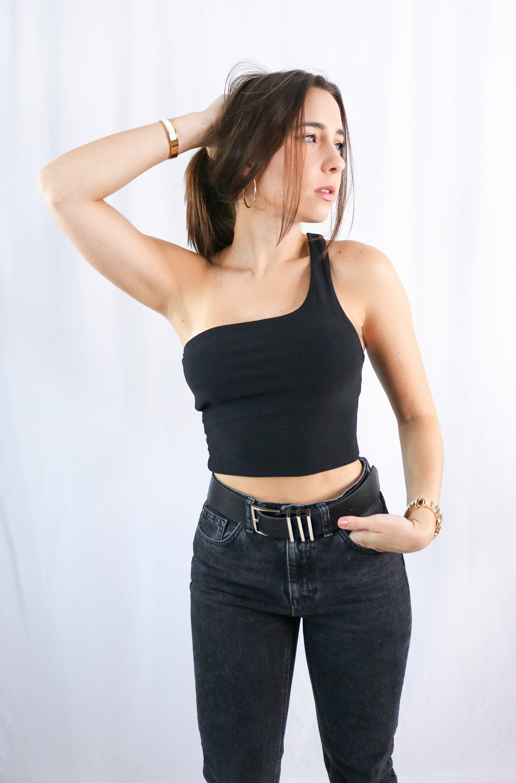 Brunette girl models a black one shoulder crop top for Scarlette The Label, an online fashion boutique for women. The black one shoulder crop top is double lined. Paired with dark denim jeans.