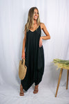 Blonde girl modeling a black boxy hi lo jumpsuit for Scarlette The Label, an online fashion boutique for women. Black jumpsuit has pockets and is lightweight and flowy. Paired with large straw bag.